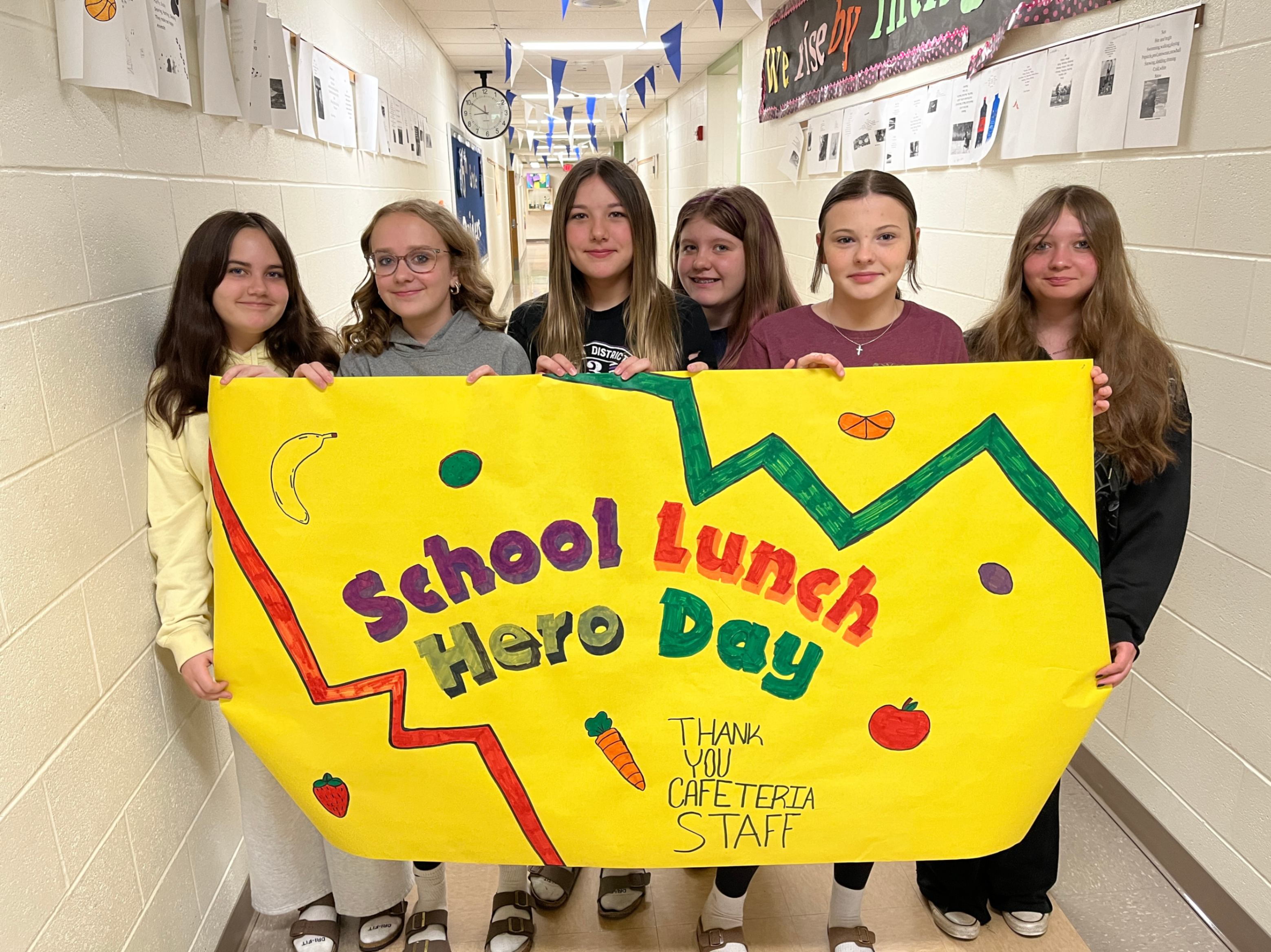 Six elementary students are holding a sign that says School Lunch Hero Day - Thank You Cafeteria Staff.